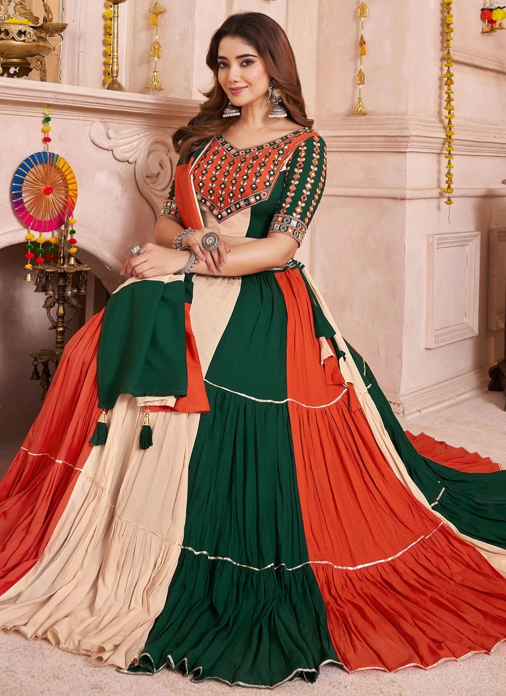 Woman wearing a traditional green and red saree with intricate patterns in a decorated room.