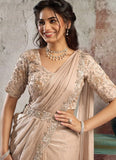 Woman wearing a beige saree with silver embroidery against a textured wall.