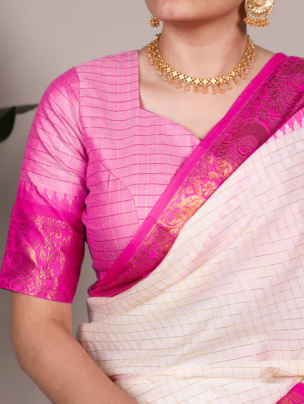 Woman wearing a pink and white saree with gold jewelry against a neutral background