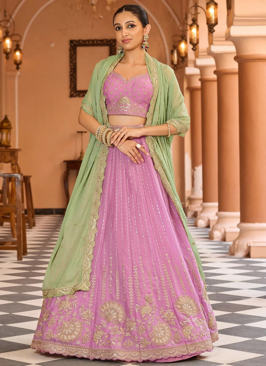 Woman in a pink and green traditional outfit standing in an elegant indoor setting.