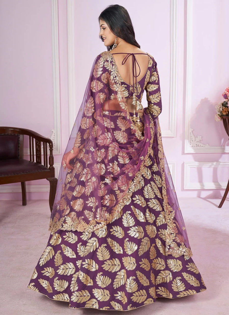 Woman wearing a purple and gold traditional outfit with a sheer dupatta in a room.