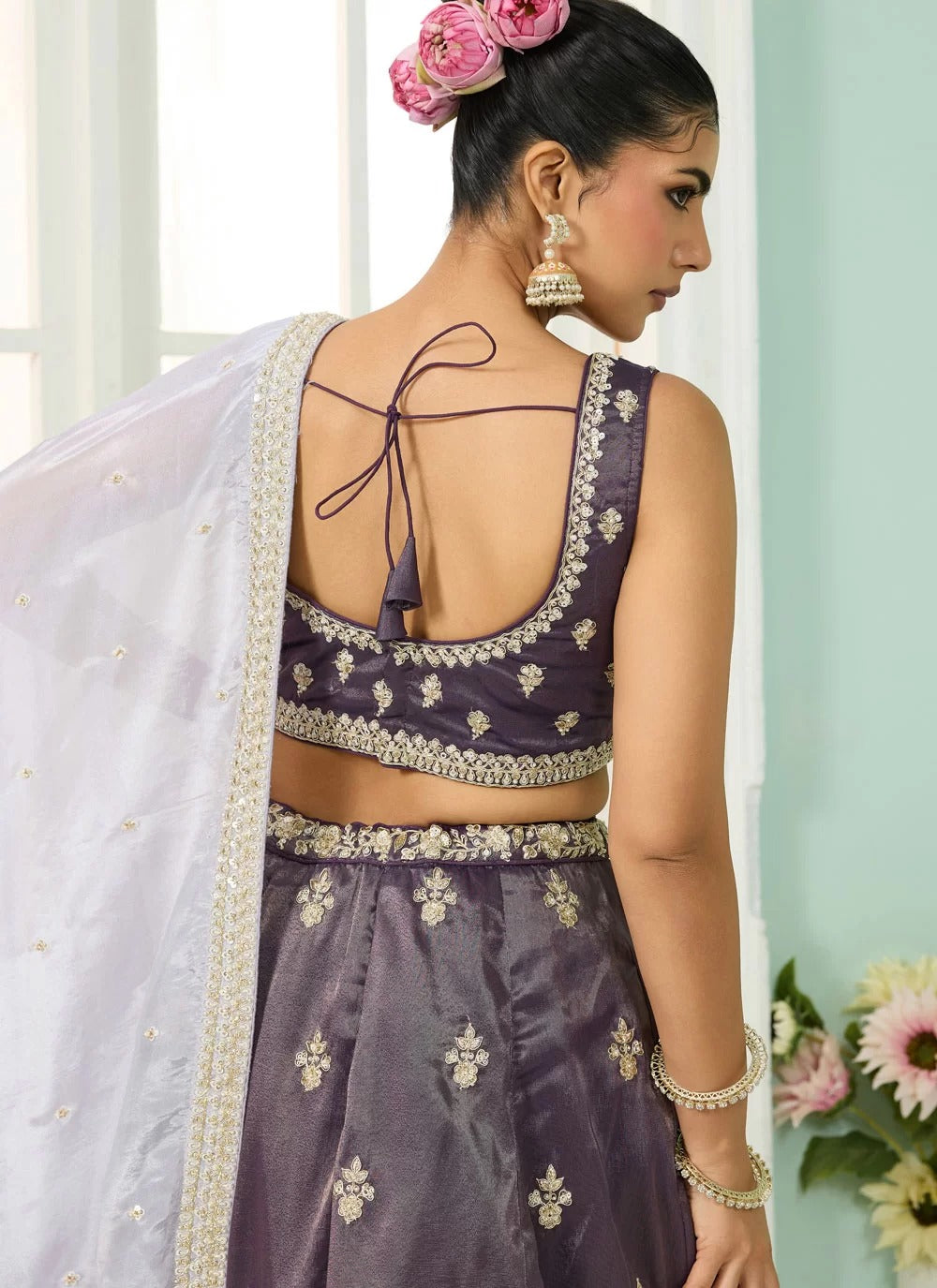 Woman wearing a traditional embroidered outfit with a white dupatta, standing against a light green wall.
