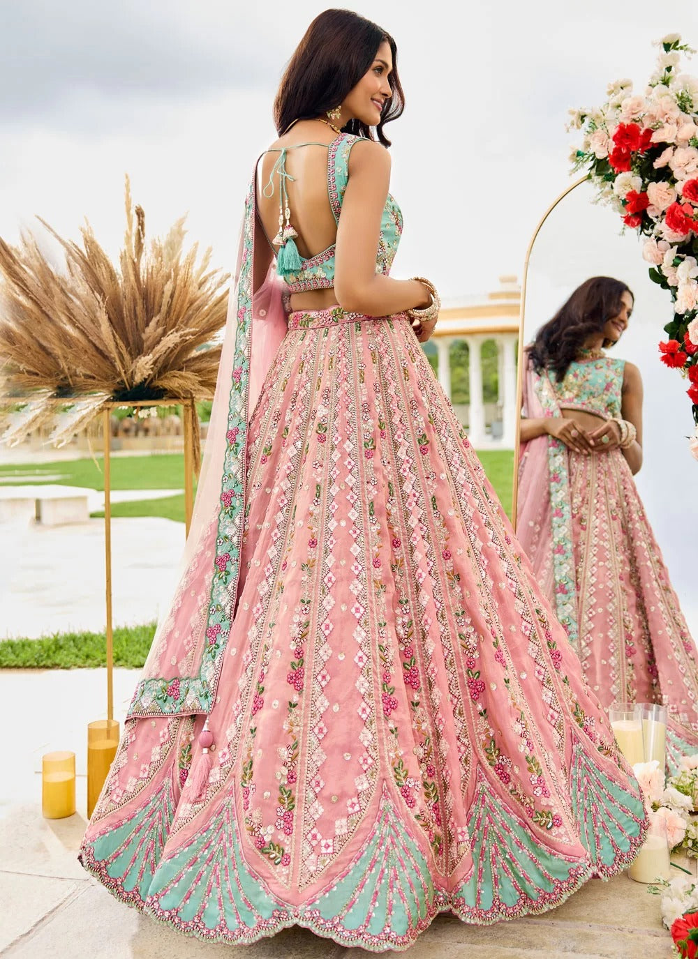 Woman in a pink and green traditional outfit standing in front of floral decorations.