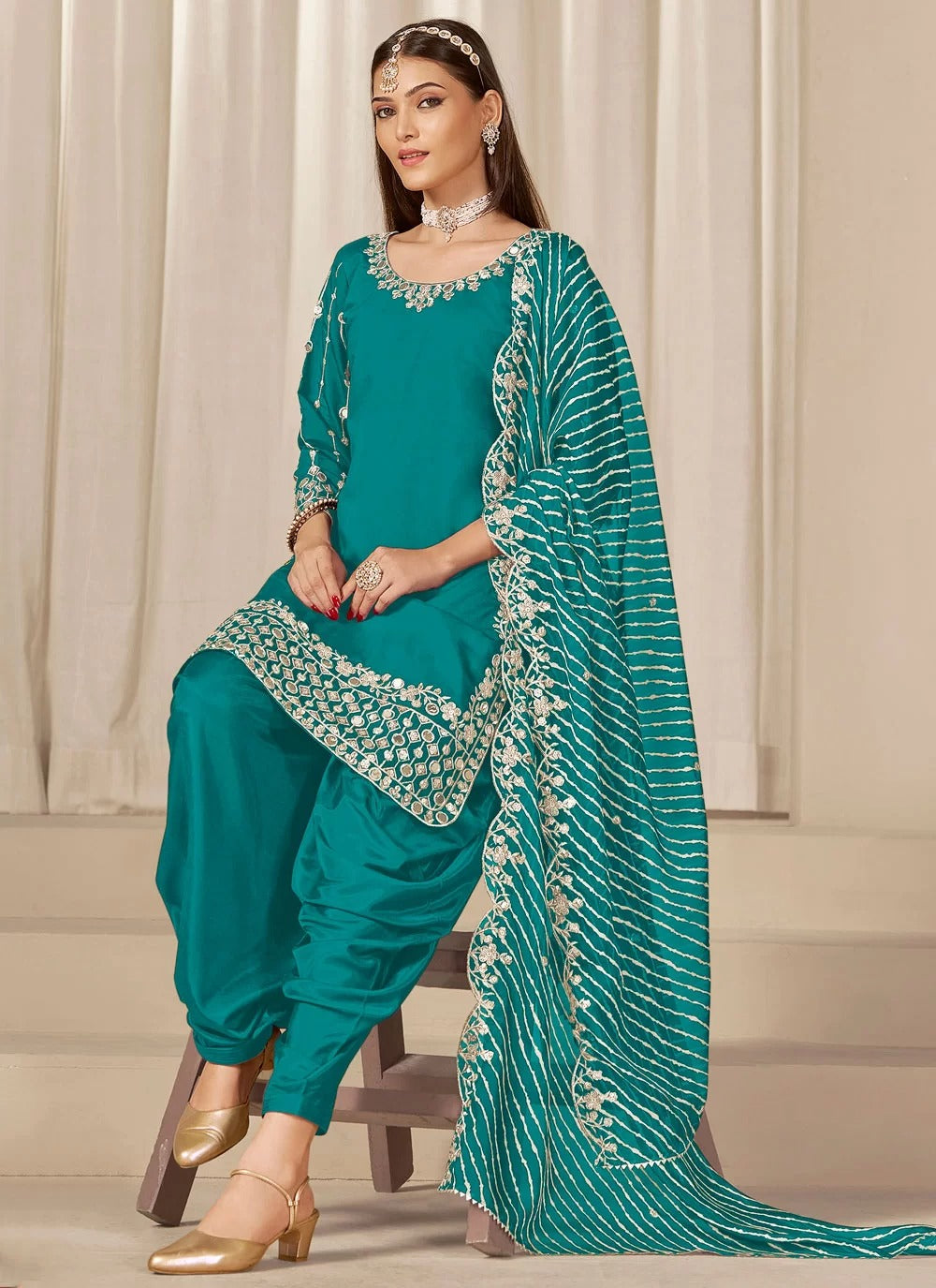 Woman wearing a teal traditional outfit with a matching dupatta against a neutral background