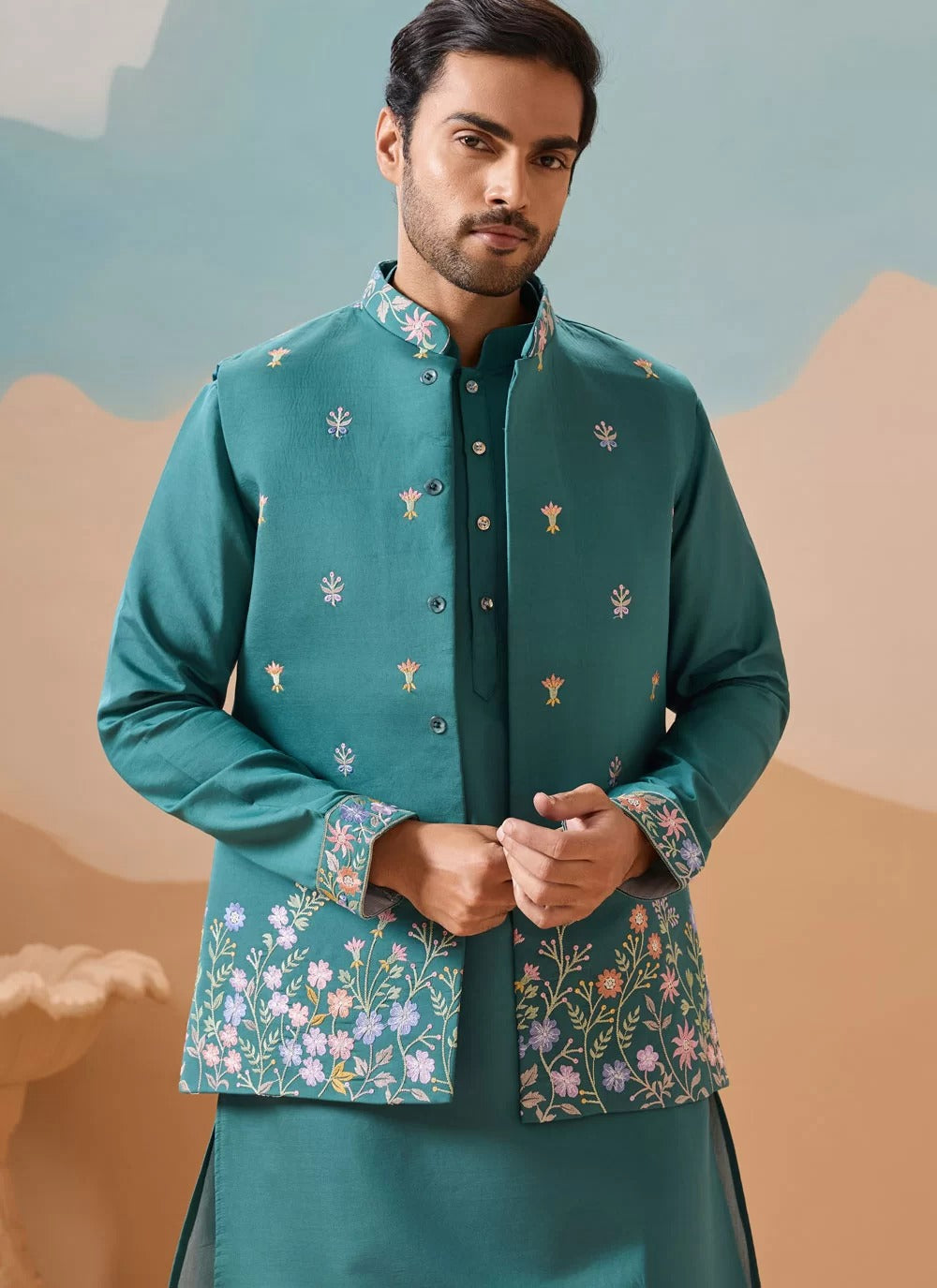 Man wearing a teal embroidered traditional outfit against a desert landscape