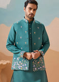 Man wearing a teal embroidered traditional outfit against a desert landscape