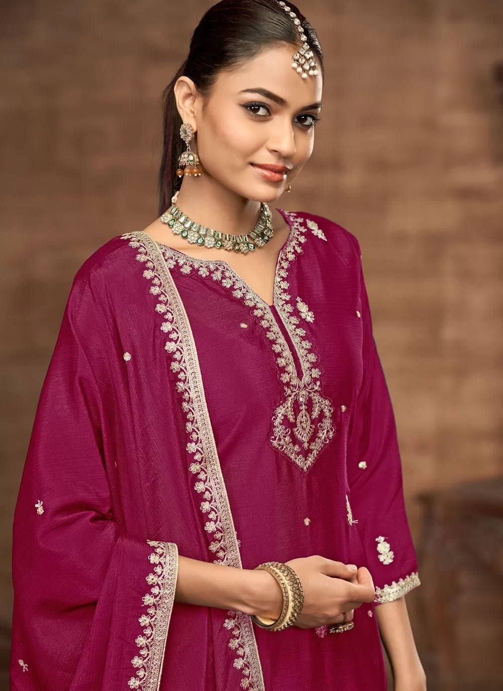 Woman wearing a pink traditional outfit with intricate embroidery against a brown background