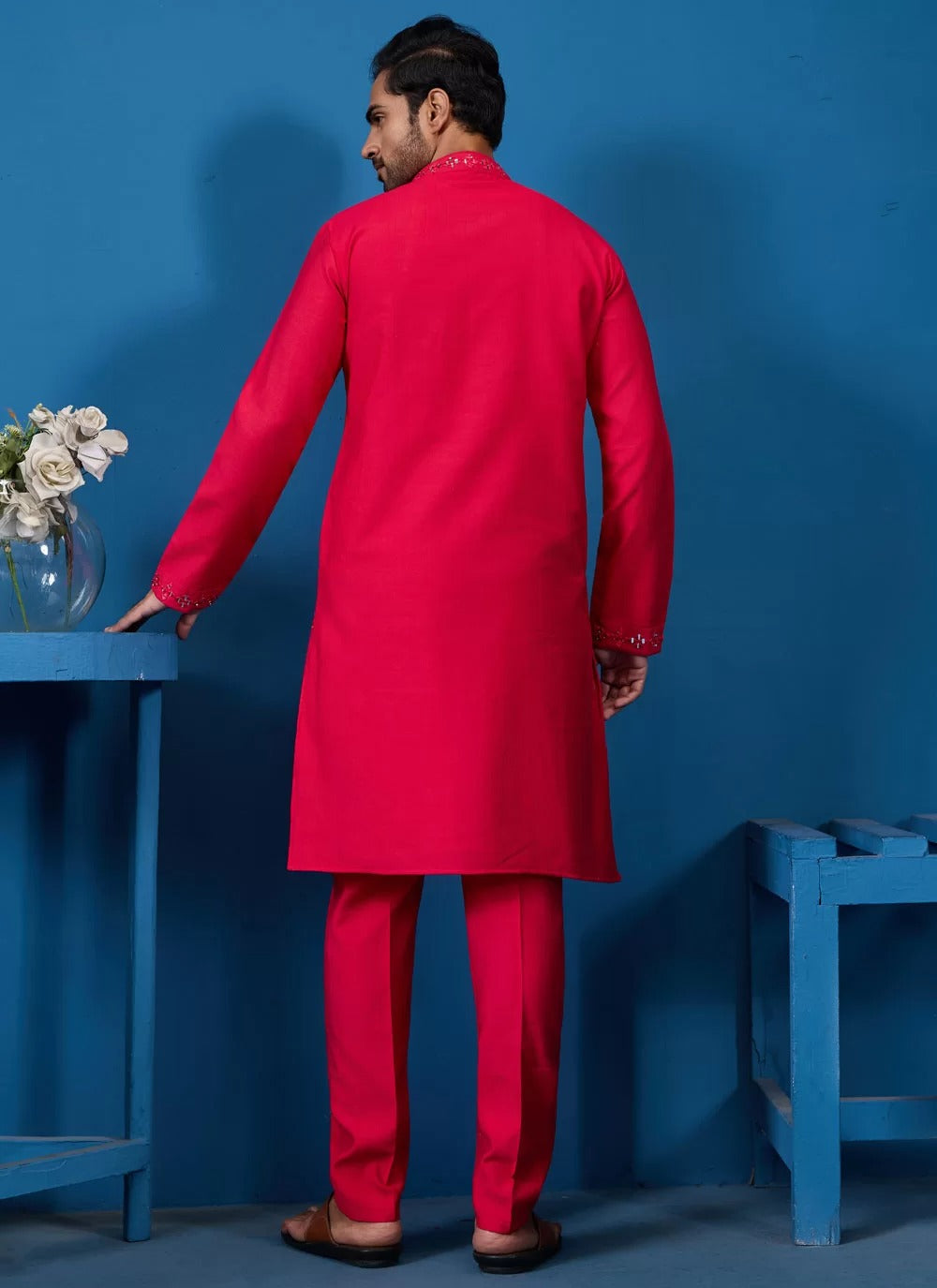 Man wearing a bright red kurta against a blue background
