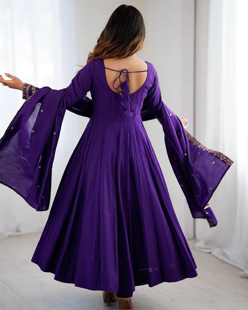 Woman wearing a purple dress with long sleeves and a backless design, standing against a white curtain.