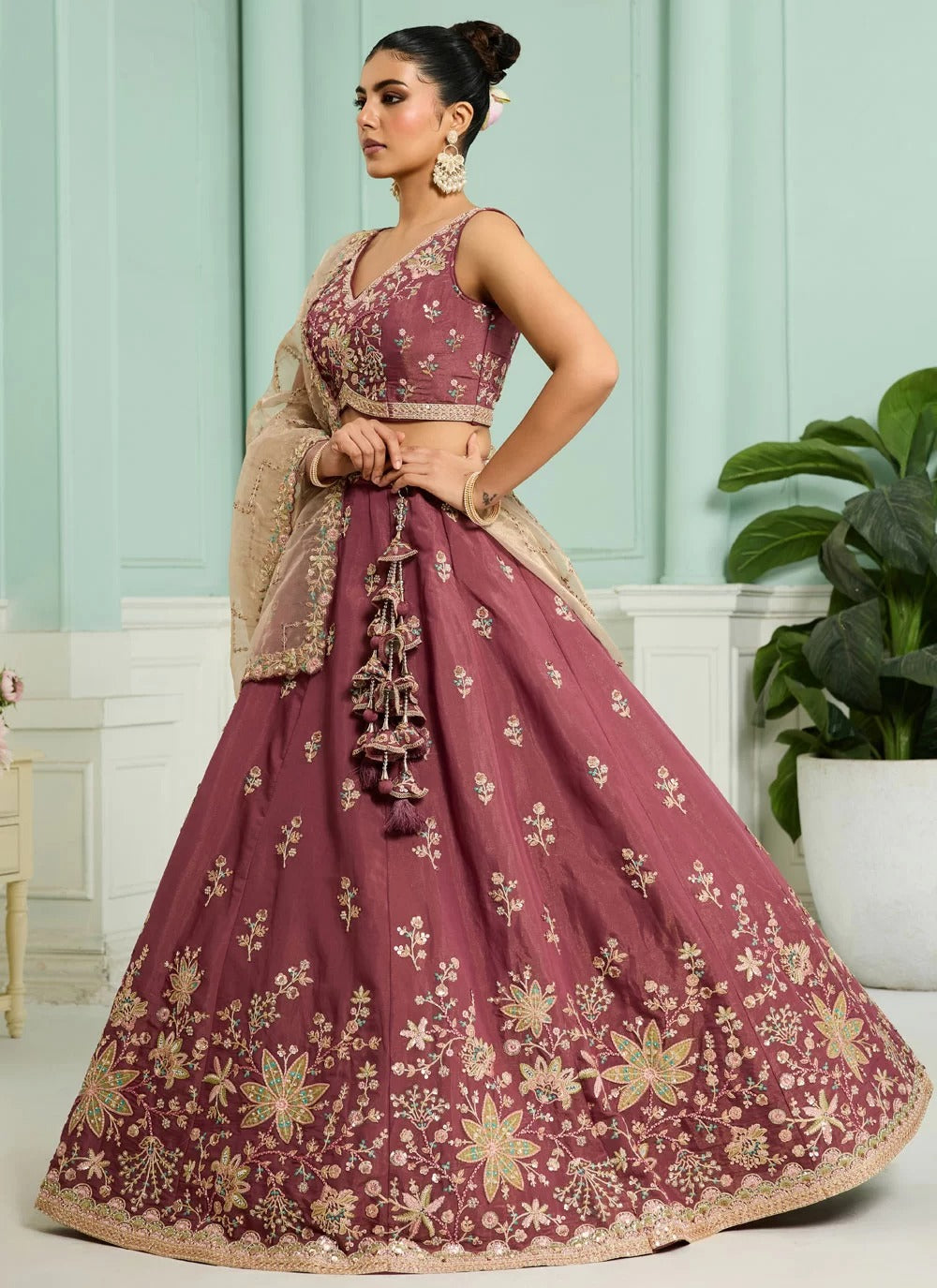 Woman in a maroon embroidered traditional outfit with gold details in an indoor setting.