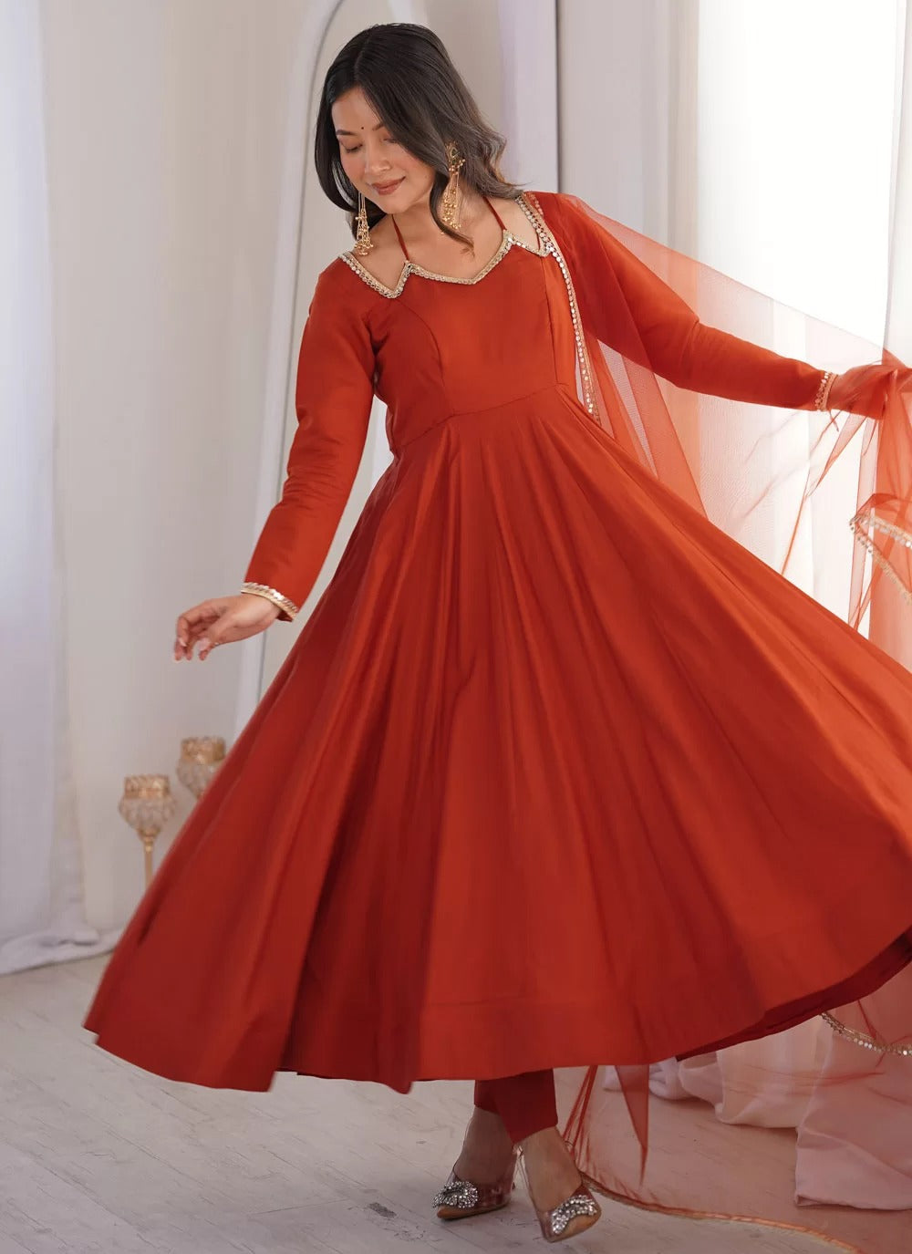 Woman in a red traditional outfit with a sheer dupatta in a bright room.