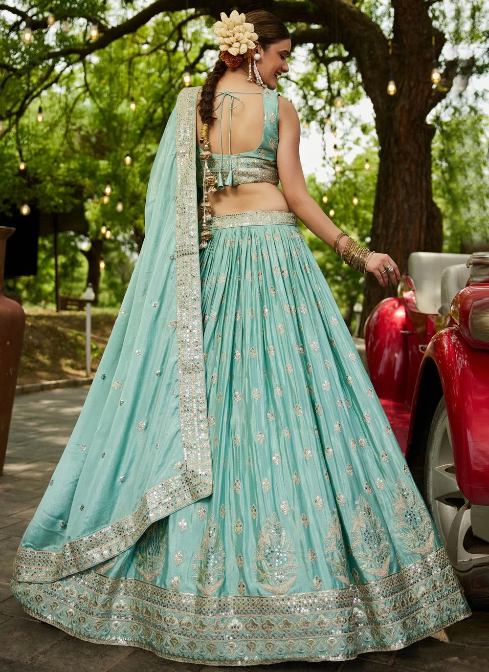 Woman in a light blue traditional outfit with a floral headpiece, standing outdoors.