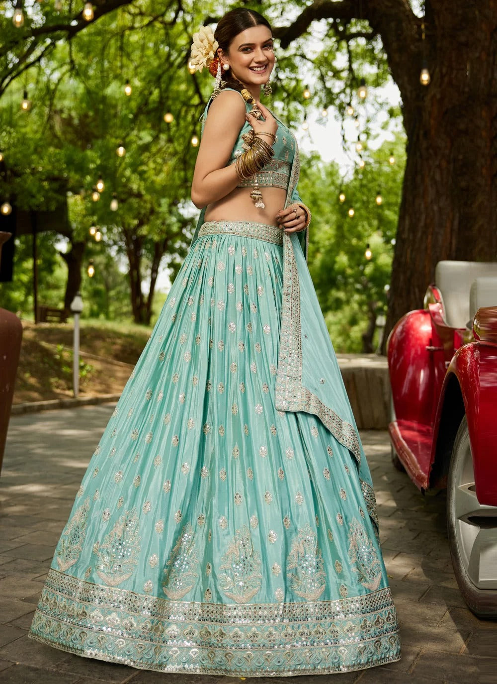 Woman in a light blue embroidered traditional outfit standing outdoors with greenery in the background.