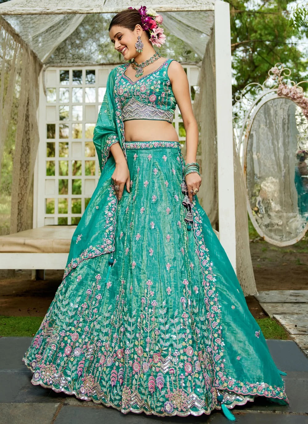 Woman in a teal embroidered traditional outfit standing outdoors.