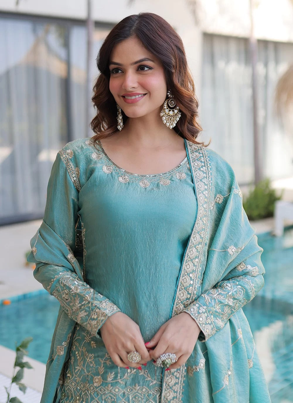 Woman wearing a teal traditional outfit with embroidery, standing outdoors.