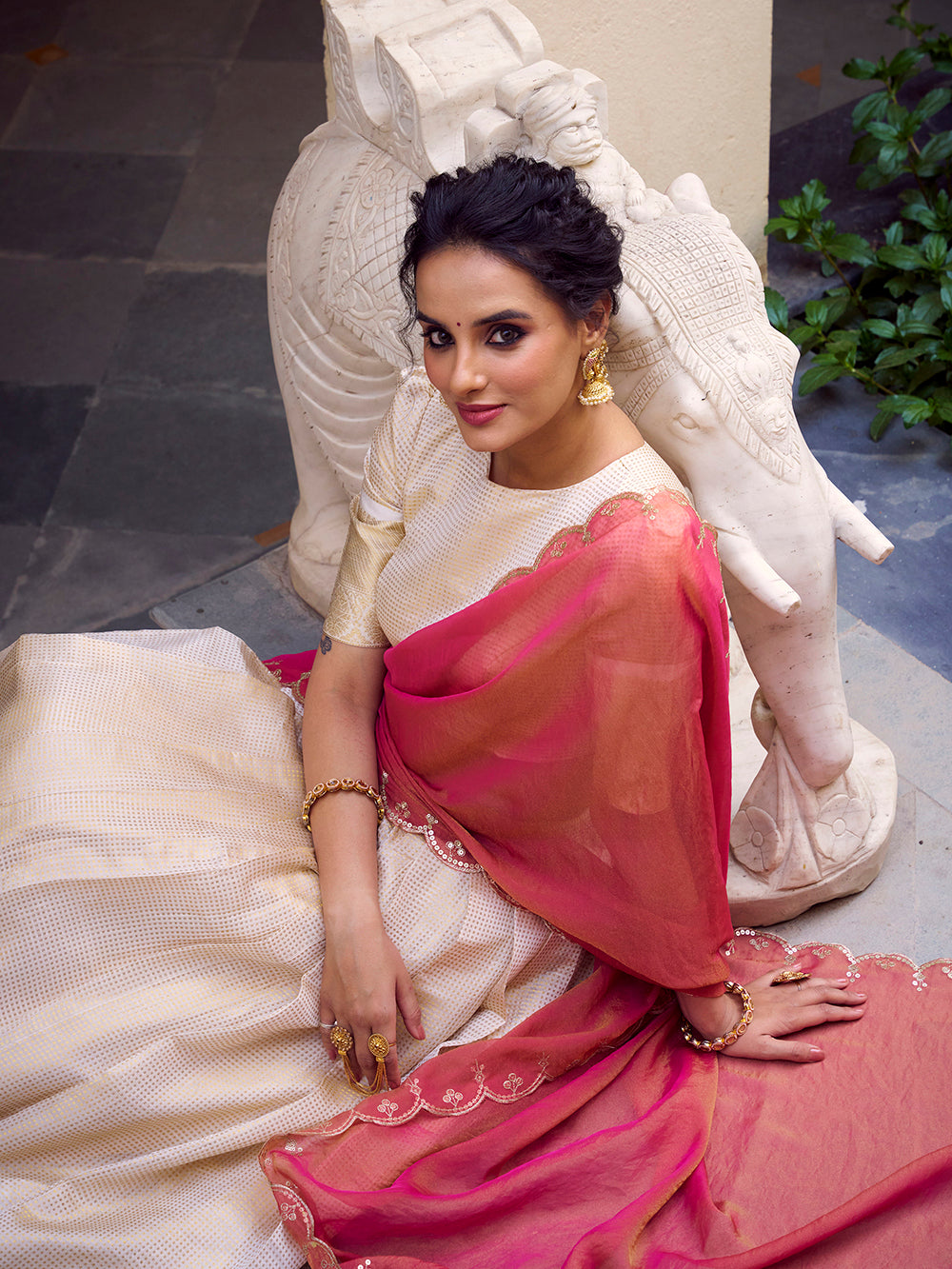 Woman in a traditional saree sitting on a decorative chair.