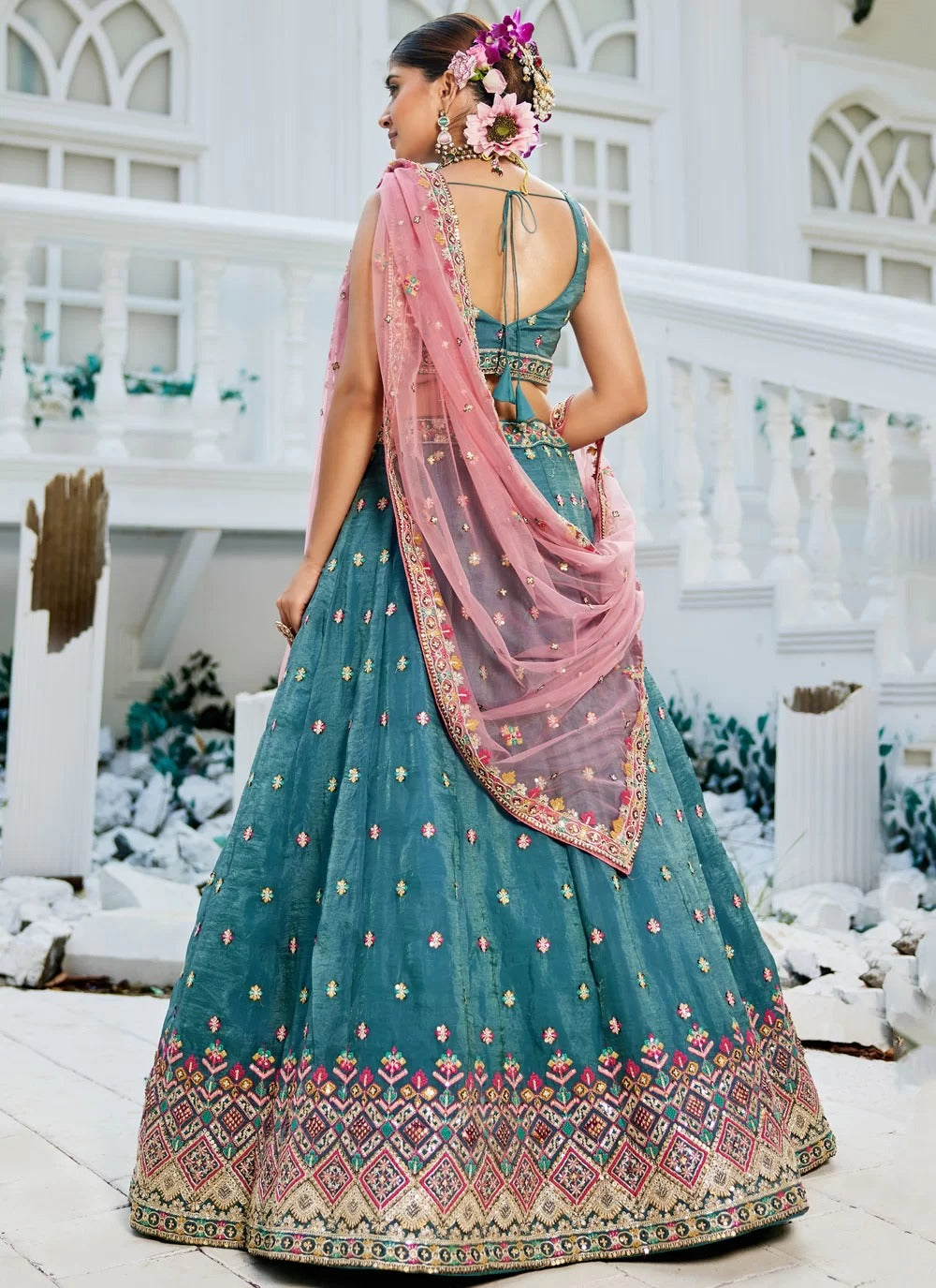 Woman in a traditional teal and pink outfit standing in a decorative setting.
