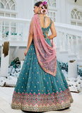 Woman in a traditional teal and pink outfit standing in a decorative setting.