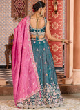 Woman in a teal embroidered saree with pink dupatta in an ornate indoor setting