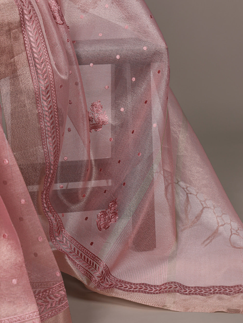 Pink embroidered fabric with intricate patterns on a gray background
