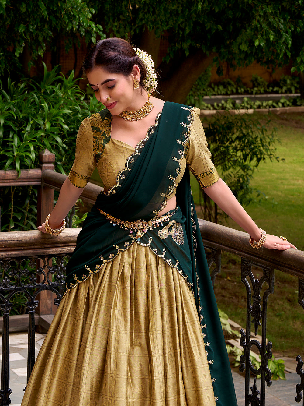 Woman in a green and gold traditional outfit standing outdoors with greenery in the background