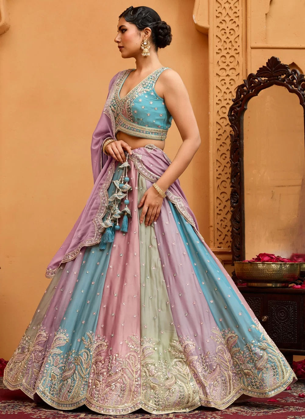 Woman wearing a traditional multicolored outfit with intricate designs in a warm-toned room.