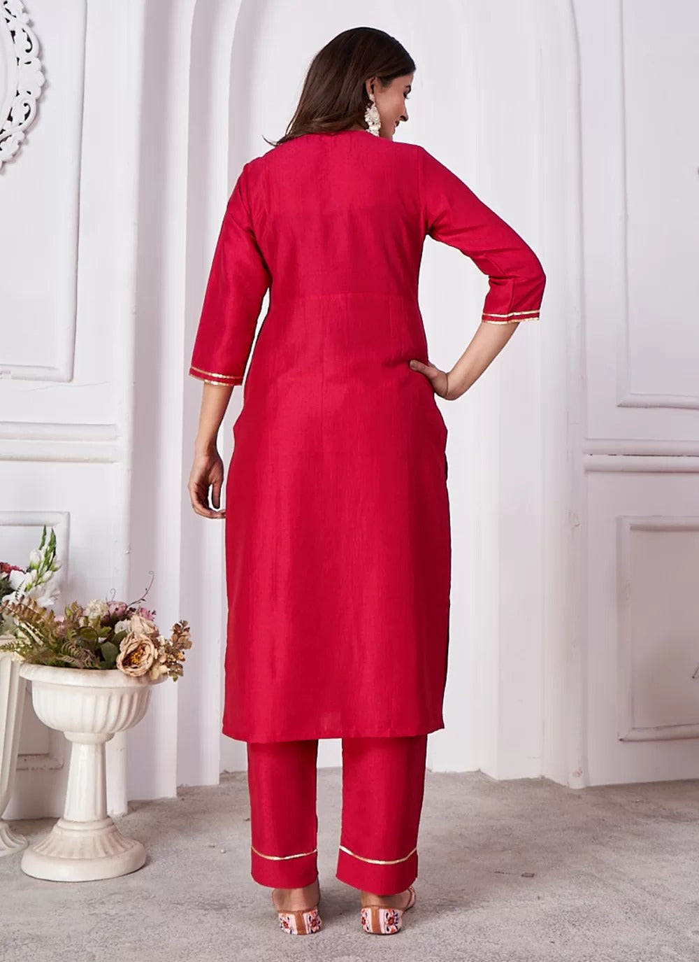 Woman wearing a red kurta with white trim in a minimalistic setting.