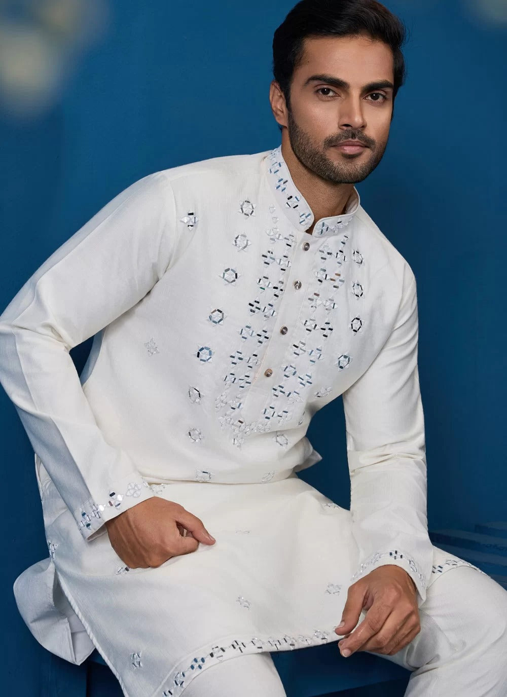 Man wearing a white embroidered traditional outfit against a blue background