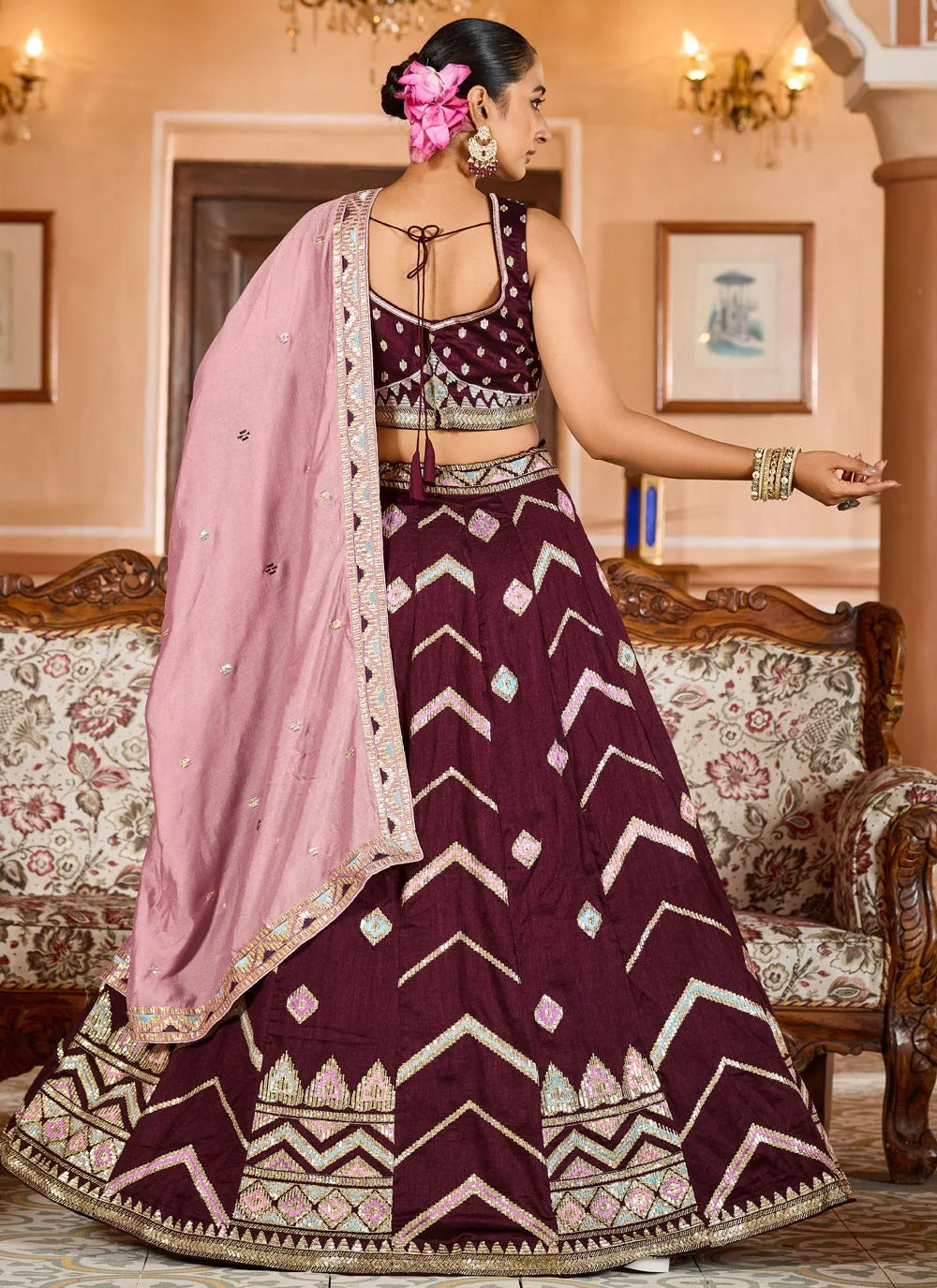 Woman in a traditional maroon and pink embroidered outfit in a decorated room.