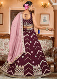 Woman in a traditional maroon and pink embroidered outfit in a decorated room.