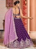 Woman in a purple and pink traditional outfit with intricate designs in a decorated room.